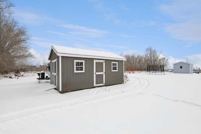 snow covered structure featuring a storage shed, a trampoline, and an outdoor structure