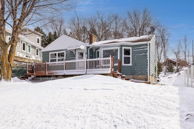 snow covered back of property with a chimney, fence, and a wooden deck