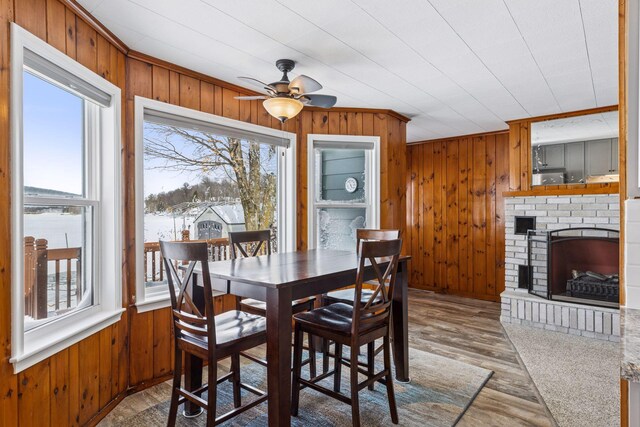 dining space with light wood-type flooring, a brick fireplace, wooden walls, and ornamental molding