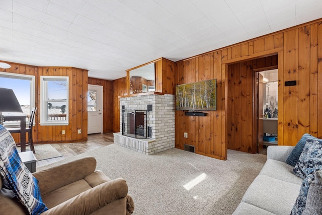 living room featuring carpet floors, a brick fireplace, visible vents, and wooden walls