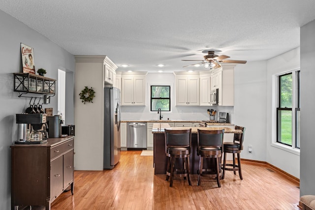 17130 Uplander Cir NW, Andover, MN 55304 - kitchen with stainless steel appliances, a sink, a breakfast bar area, light wood-style flooring, and a ceiling fan