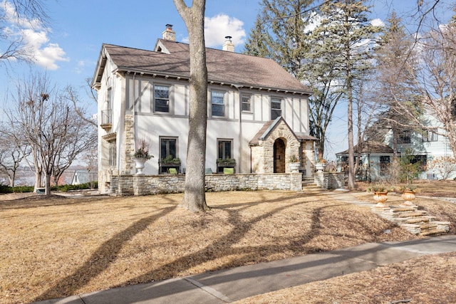 view of front facade with stone siding, a chimney, roof with shingles, and stucco siding