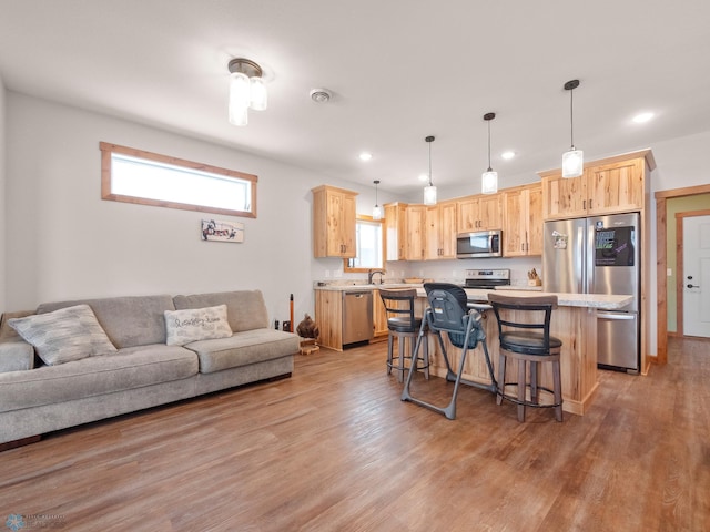 kitchen featuring appliances with stainless steel finishes, light brown cabinetry, a kitchen bar, a center island, and light hardwood / wood-style flooring