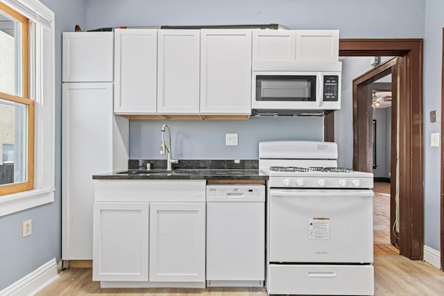 kitchen featuring white cabinetry, sink, dark stone countertops, white appliances, and light hardwood / wood-style flooring