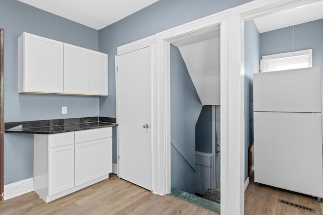 kitchen with white refrigerator, white cabinetry, light hardwood / wood-style floors, and dark stone countertops