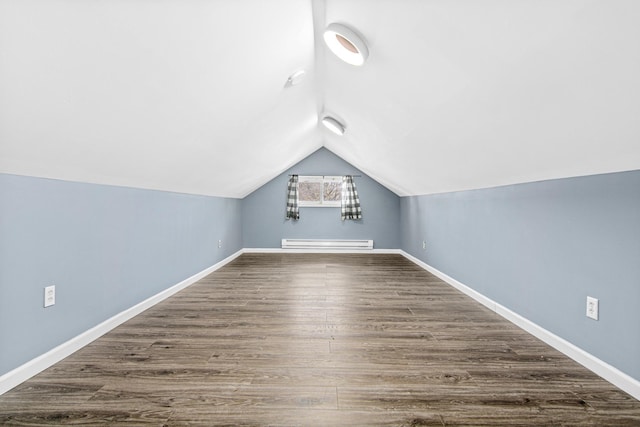 additional living space featuring dark wood-type flooring, vaulted ceiling, and a baseboard heating unit