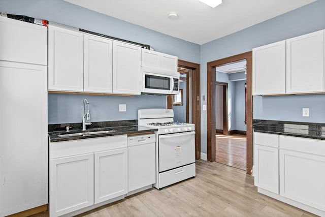 kitchen featuring sink, light hardwood / wood-style flooring, white appliances, dark stone counters, and white cabinets