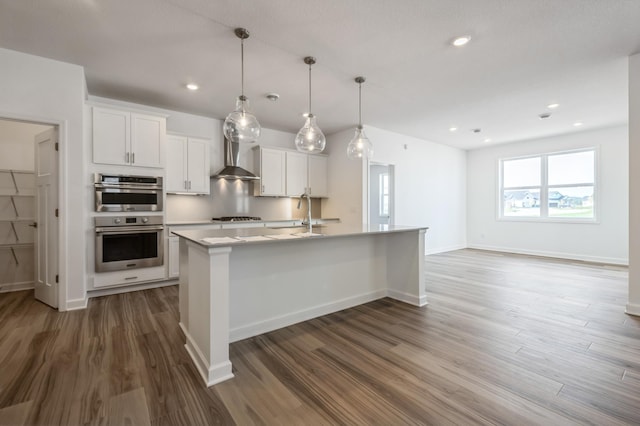 kitchen featuring pendant lighting, stainless steel appliances, a center island with sink, and white cabinets