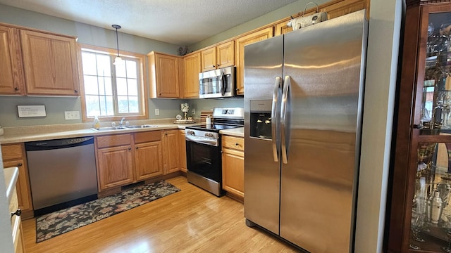 kitchen featuring a sink, a textured ceiling, light wood-style floors, appliances with stainless steel finishes, and light countertops