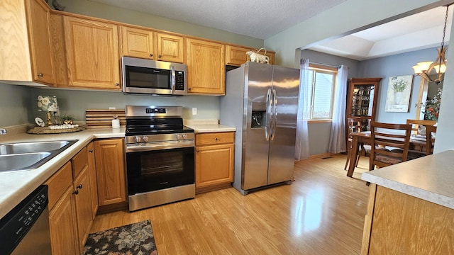 kitchen with light wood finished floors, a chandelier, light countertops, appliances with stainless steel finishes, and a sink