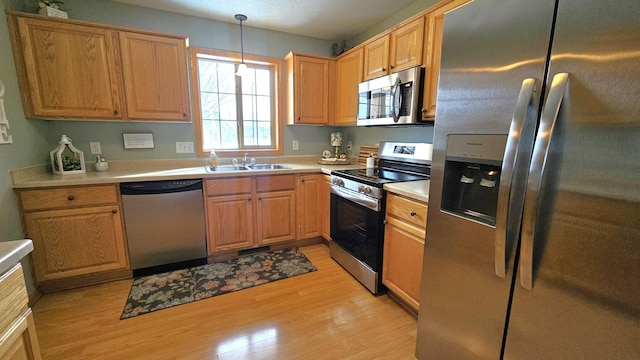 kitchen with a sink, stainless steel appliances, light wood-style floors, light countertops, and hanging light fixtures