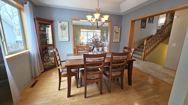 dining area with visible vents, light wood-style flooring, stairs, and an inviting chandelier