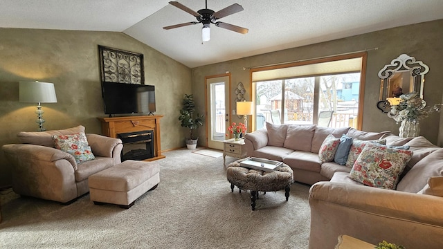 living area featuring lofted ceiling, carpet floors, a glass covered fireplace, a textured ceiling, and a ceiling fan