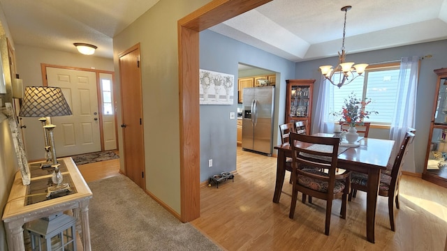 dining space featuring baseboards, light wood-style floors, a textured ceiling, a raised ceiling, and a notable chandelier