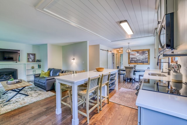 kitchen with wood ceiling, light hardwood / wood-style floors, a brick fireplace, decorative light fixtures, and a barn door