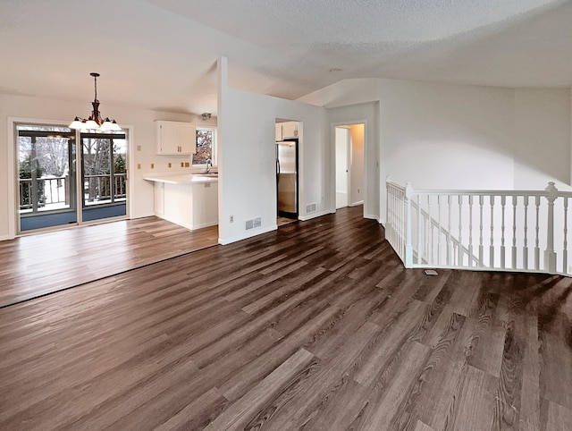 unfurnished living room with sink, vaulted ceiling, dark hardwood / wood-style floors, and a chandelier