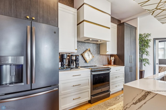 kitchen featuring white cabinetry, light stone counters, light wood-type flooring, stainless steel appliances, and backsplash