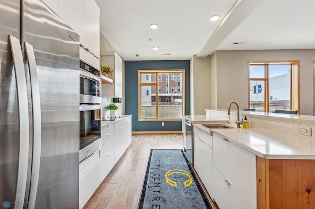 kitchen with sink, light hardwood / wood-style flooring, appliances with stainless steel finishes, a kitchen island with sink, and white cabinets