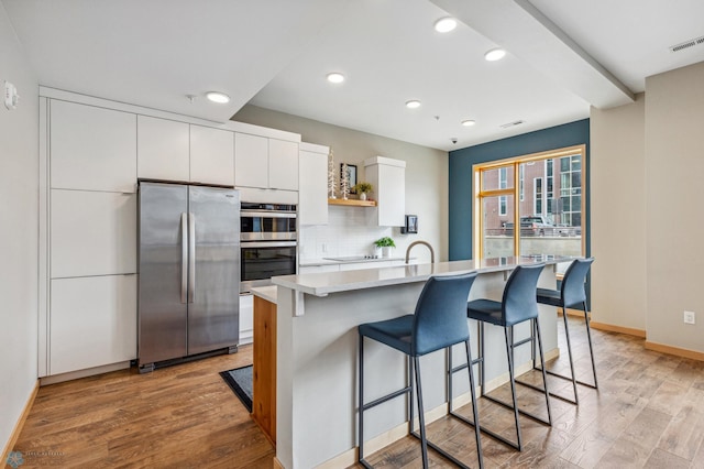 kitchen featuring appliances with stainless steel finishes, white cabinetry, a kitchen breakfast bar, a kitchen island with sink, and light wood-type flooring