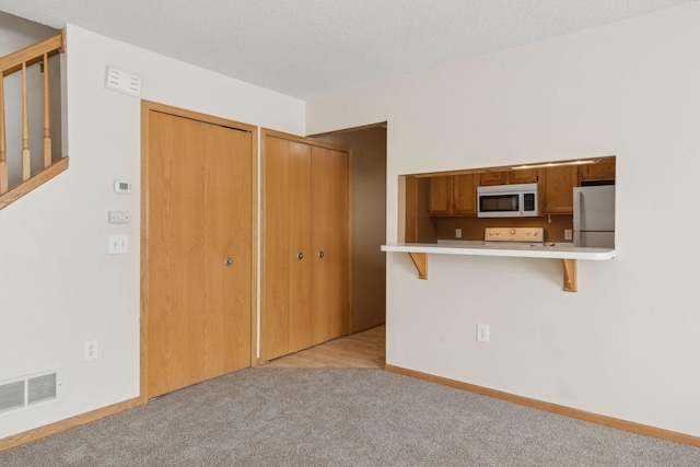 interior space featuring refrigerator, a textured ceiling, a kitchen bar, light colored carpet, and kitchen peninsula