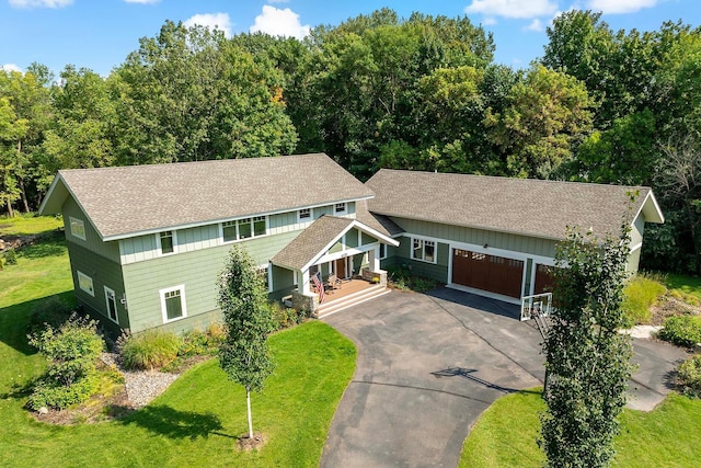 craftsman-style home featuring a porch, aphalt driveway, a garage, a shingled roof, and a front yard