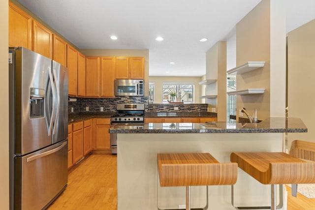 kitchen with dark stone countertops, stainless steel appliances, a kitchen breakfast bar, decorative backsplash, and kitchen peninsula