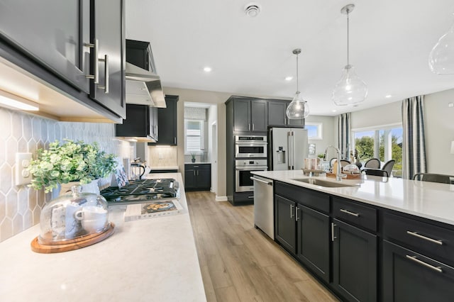 kitchen with decorative light fixtures, sink, decorative backsplash, stainless steel appliances, and light wood-type flooring