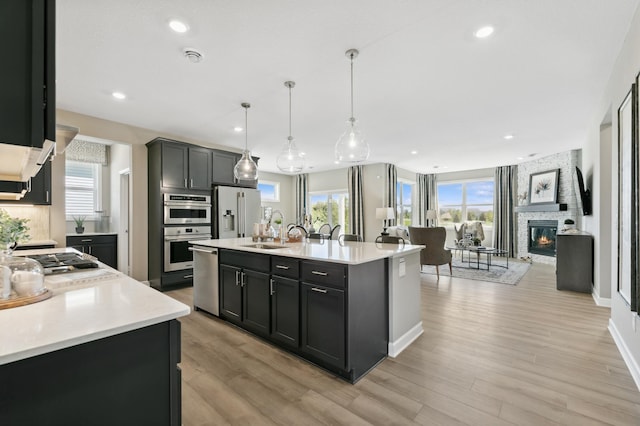 kitchen with appliances with stainless steel finishes, a fireplace, a kitchen island with sink, and hanging light fixtures