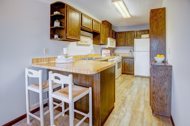 kitchen with light countertops, a peninsula, white appliances, a textured ceiling, and a sink