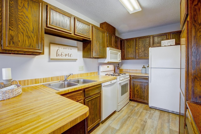 kitchen with a textured ceiling, white appliances, light wood-style floors, and a sink