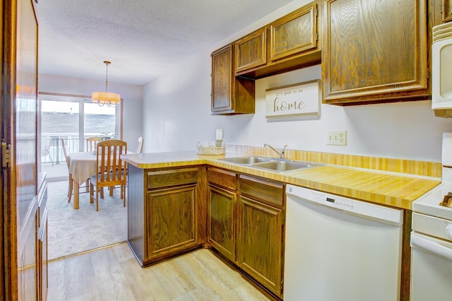 kitchen with light wood finished floors, light countertops, a peninsula, white appliances, and a sink