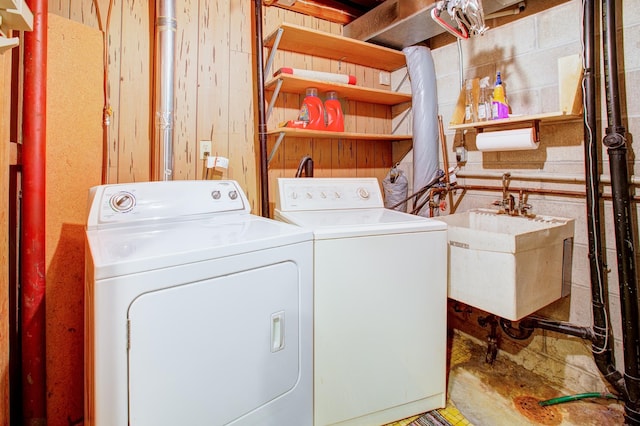 clothes washing area with wooden walls, washer and dryer, and a sink