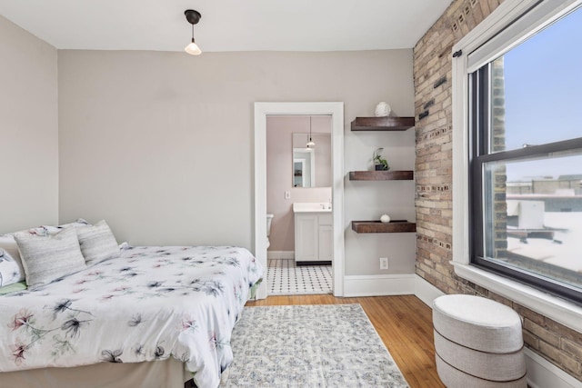 bedroom with brick wall, connected bathroom, and light wood-type flooring