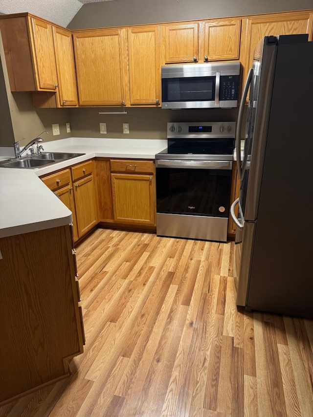 kitchen with vaulted ceiling, appliances with stainless steel finishes, sink, and light hardwood / wood-style flooring