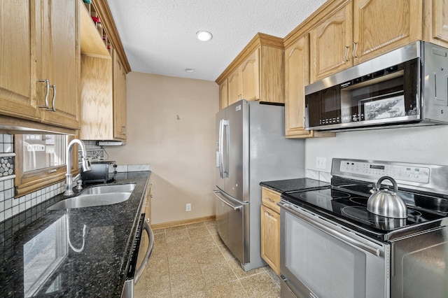 kitchen with a sink, a textured ceiling, dark stone counters, appliances with stainless steel finishes, and baseboards