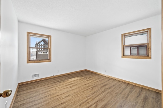 spare room with a textured ceiling, wood finished floors, visible vents, and baseboards