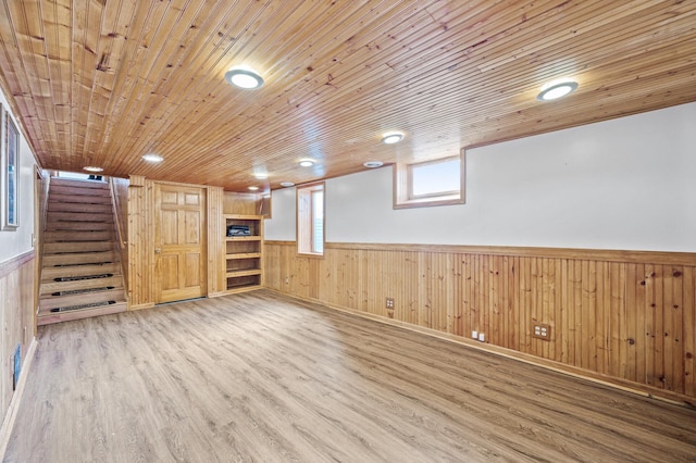 below grade area with a wainscoted wall, wood finished floors, wooden ceiling, and stairs