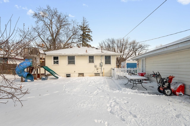 snow covered house featuring a playground and fence