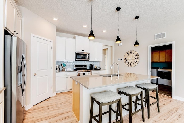 kitchen with white cabinetry, appliances with stainless steel finishes, sink, and a center island with sink