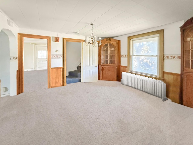205 Adams St, Hutchinson, MN 55350 - carpeted spare room featuring radiator, a chandelier, arched walkways, wainscoting, and stairs