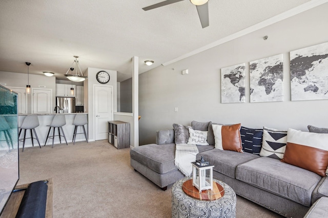 living area with a textured ceiling, crown molding, a ceiling fan, and light colored carpet