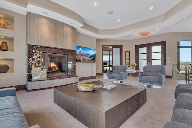 living room with a tray ceiling, a healthy amount of sunlight, a large fireplace, and french doors