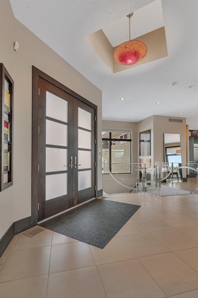 tiled entryway with french doors, a tray ceiling, and a textured ceiling