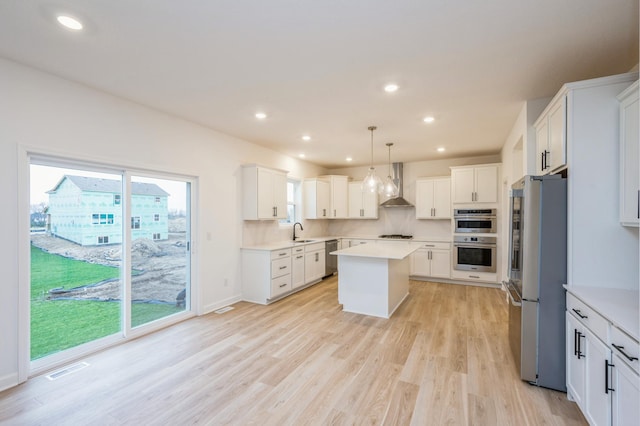 kitchen featuring appliances with stainless steel finishes, a center island, white cabinets, decorative light fixtures, and wall chimney exhaust hood