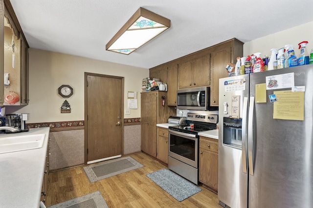 kitchen with appliances with stainless steel finishes, sink, and light wood-type flooring