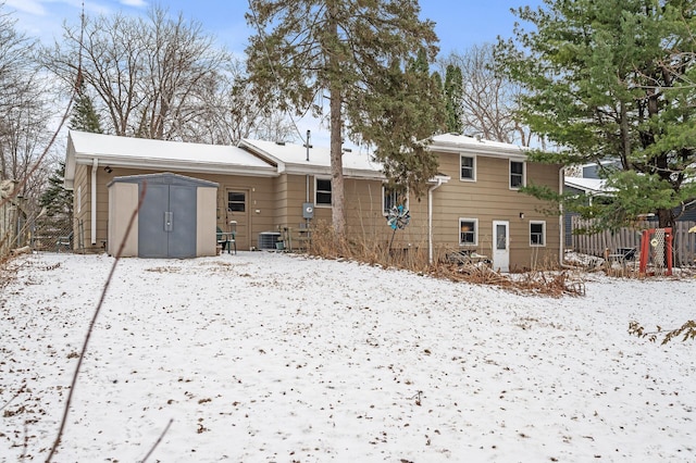 snow covered rear of property with central AC unit and a shed