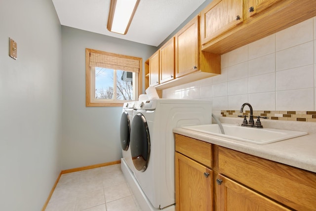 laundry area with sink, light tile patterned floors, washing machine and dryer, and cabinets