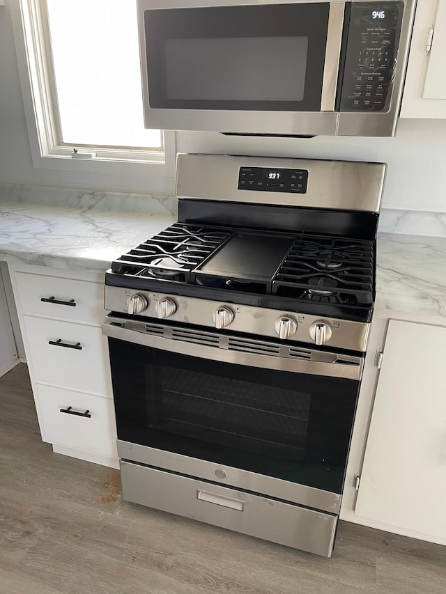 kitchen featuring appliances with stainless steel finishes, white cabinets, light stone countertops, hardwood / wood-style floors, and backsplash