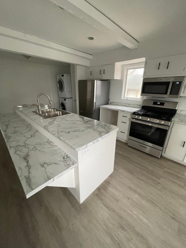 kitchen featuring sink, stacked washer / dryer, white cabinets, and appliances with stainless steel finishes