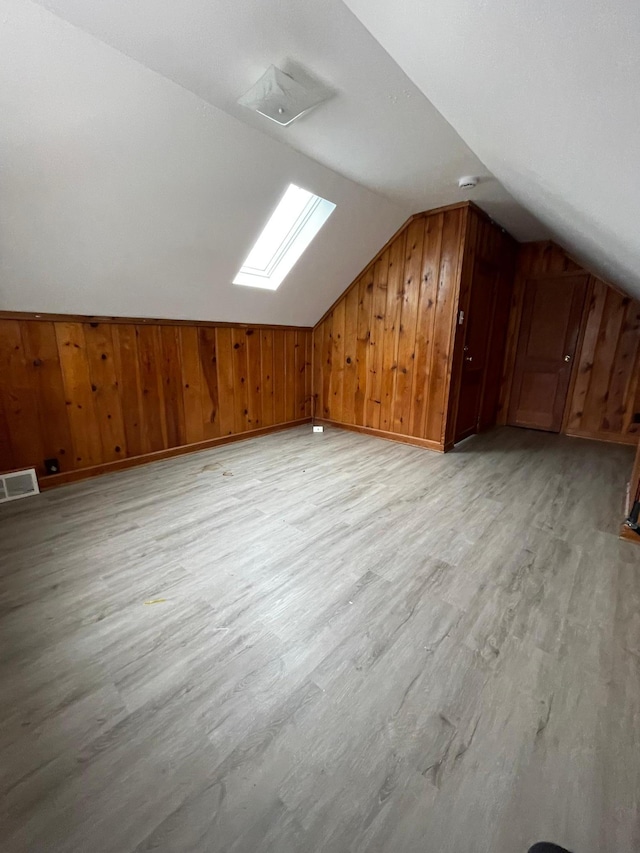 bonus room with lofted ceiling with skylight, wood walls, and light hardwood / wood-style flooring